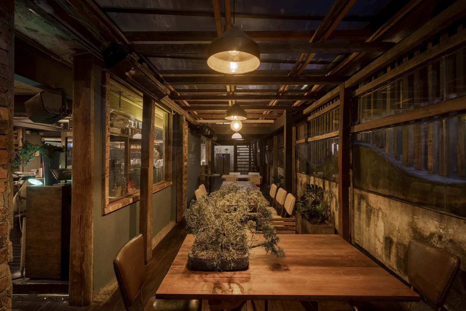 Mesa comunal de Izakaya con bonsai central y vigas de madera